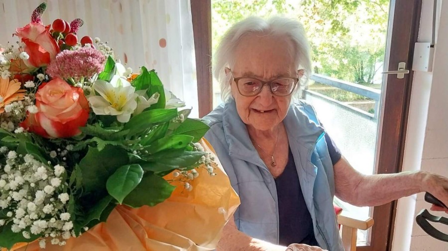 Eine ältere Dame feiert ihren 100. Geburtstag mit Blumen und Freude.
