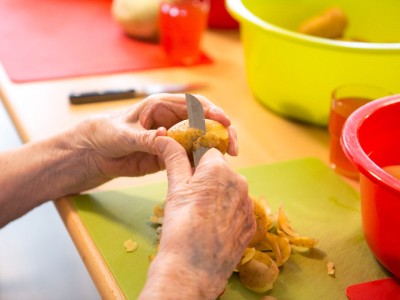 Eine ältere Person schält in einem Seniorenhaus Kartoffeln.